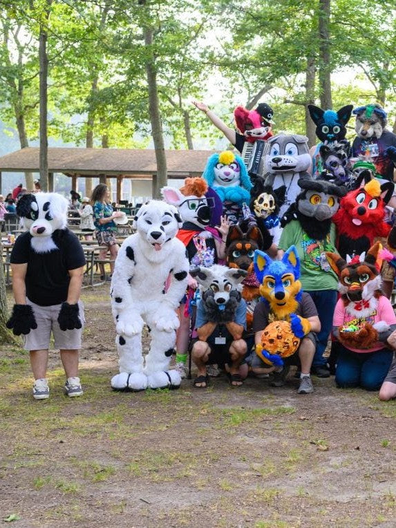 Group of people in furry costumes including black white border collie posing outdoors with trees in the background
