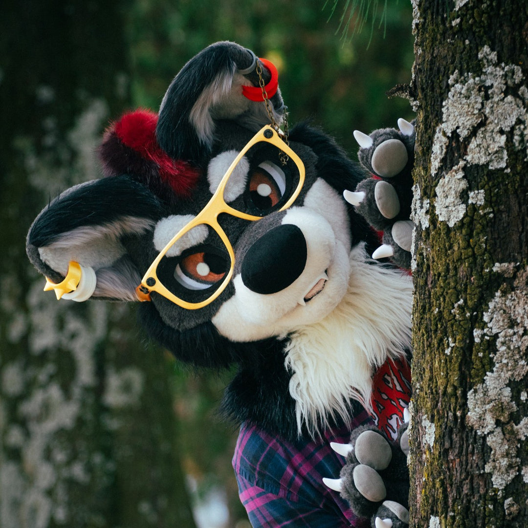 A person wearing wolf fursuit head in yellow glasses stanfing near tree