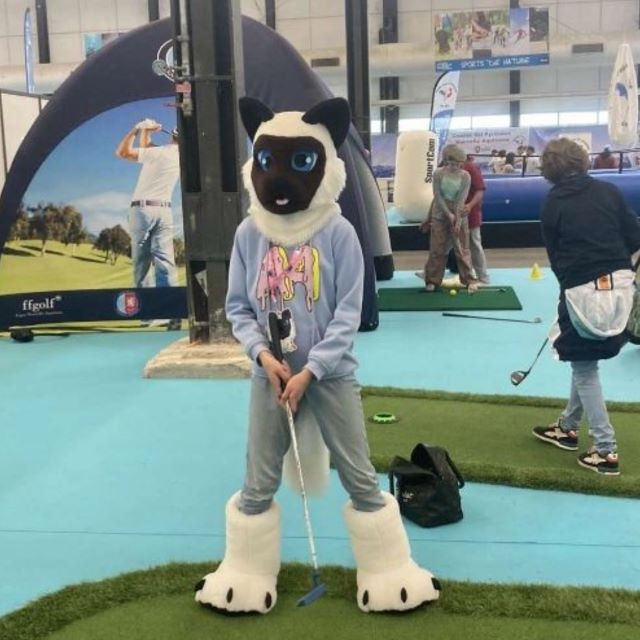 Kid in a Siamese cat fursuit head, hand paws, and feet paws at a mini golf course