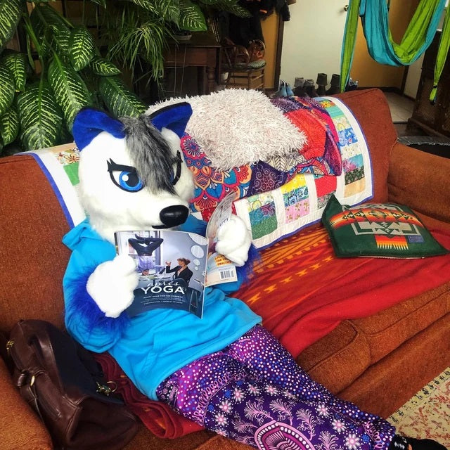 Kid wearing a white wolf fursuit while reading a newspaper on a sofa